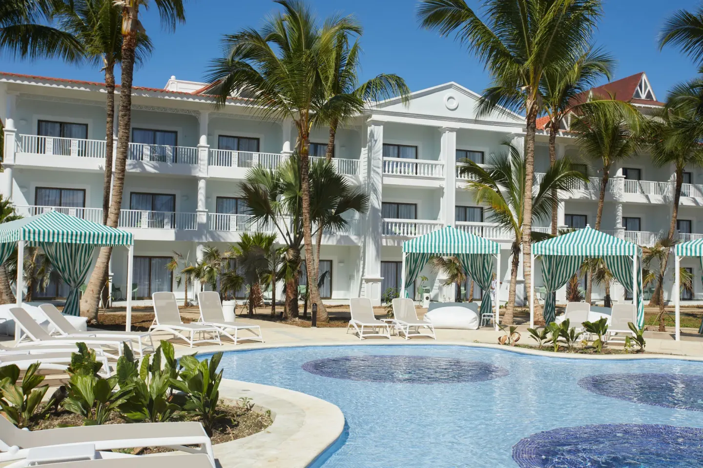 Quiet pool with striped cabanas and white balconies at Bahia Principe Explore Esmeralda.