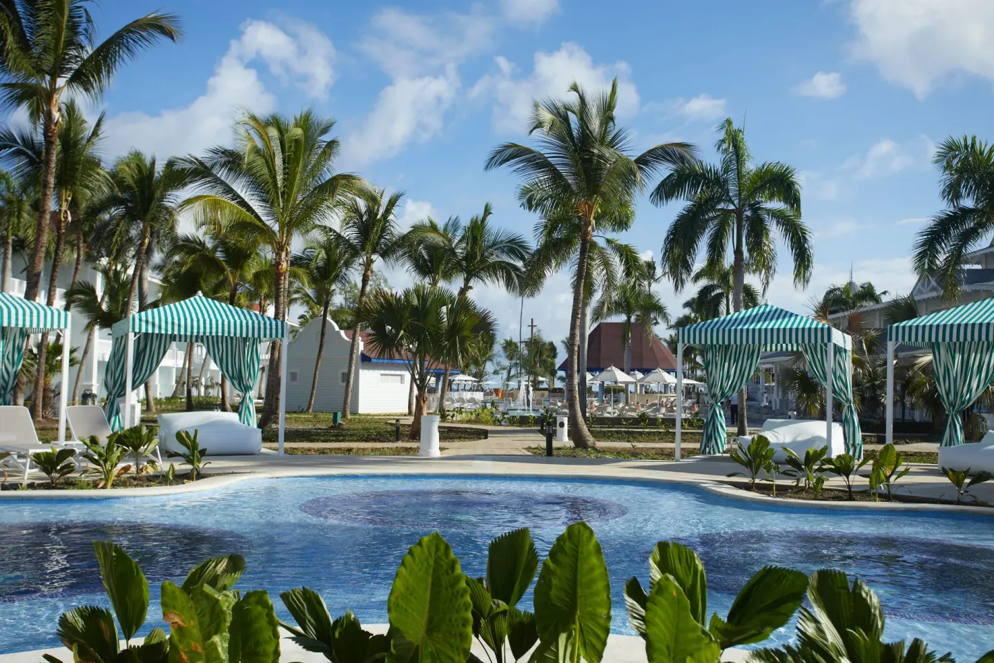 Small pool area with striped cabanas and palms at Bahia Principe Explore Esmeralda.