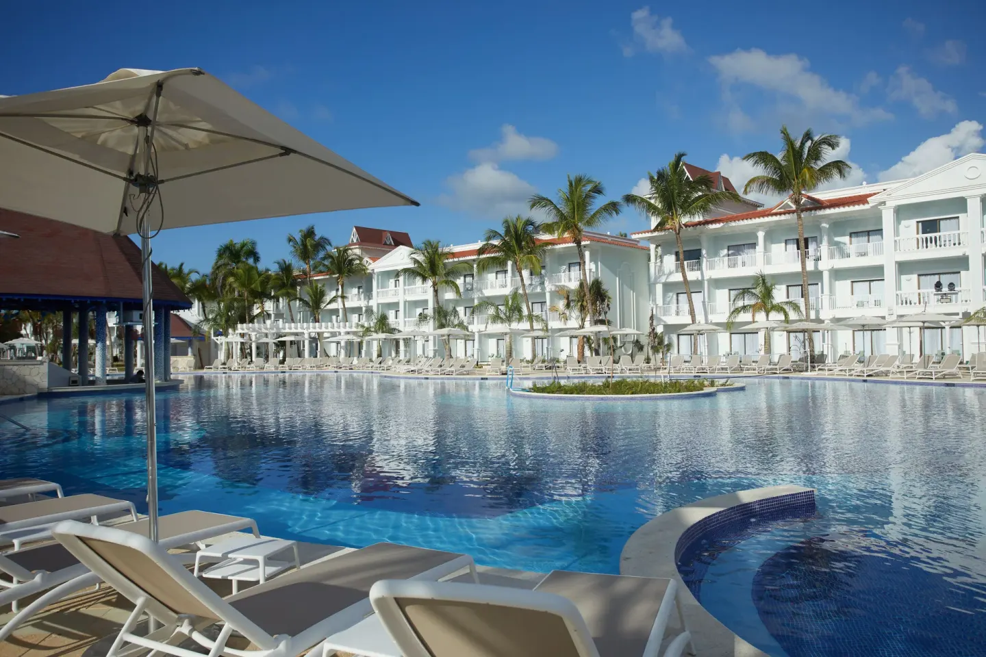 Sunny pool with loungers, palms, and white buildings at Bahia Principe Explore Esmeralda.