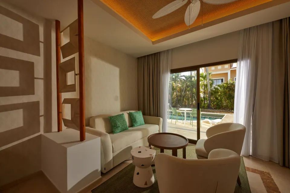 A Junior Suite at Bahia Principe Explore Esmeralda has a sofa and chairs by glass doors to the swim-up terrace.
