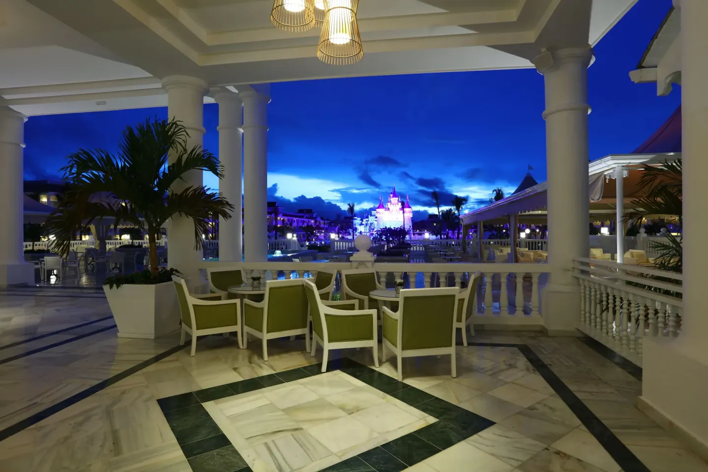 Covered terrace seating at Bahia Principe Explore Legend overlooking the illuminated resort at dusk.
