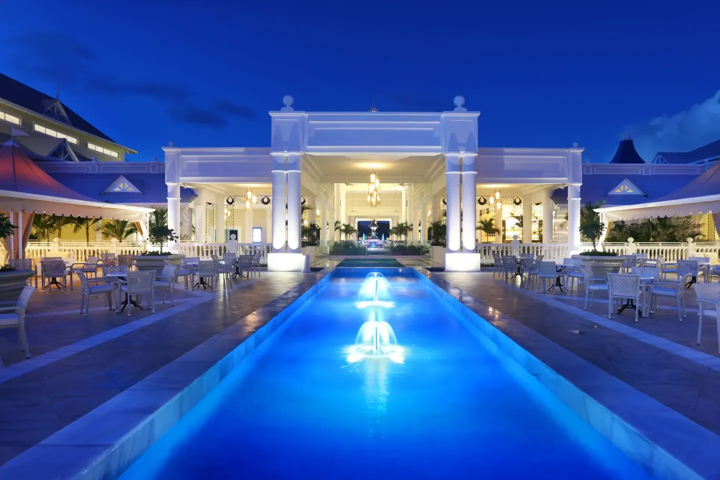 Night view of Bahia Principe Explore Legend with a glowing blue pool channel leading to a lit pavilion.