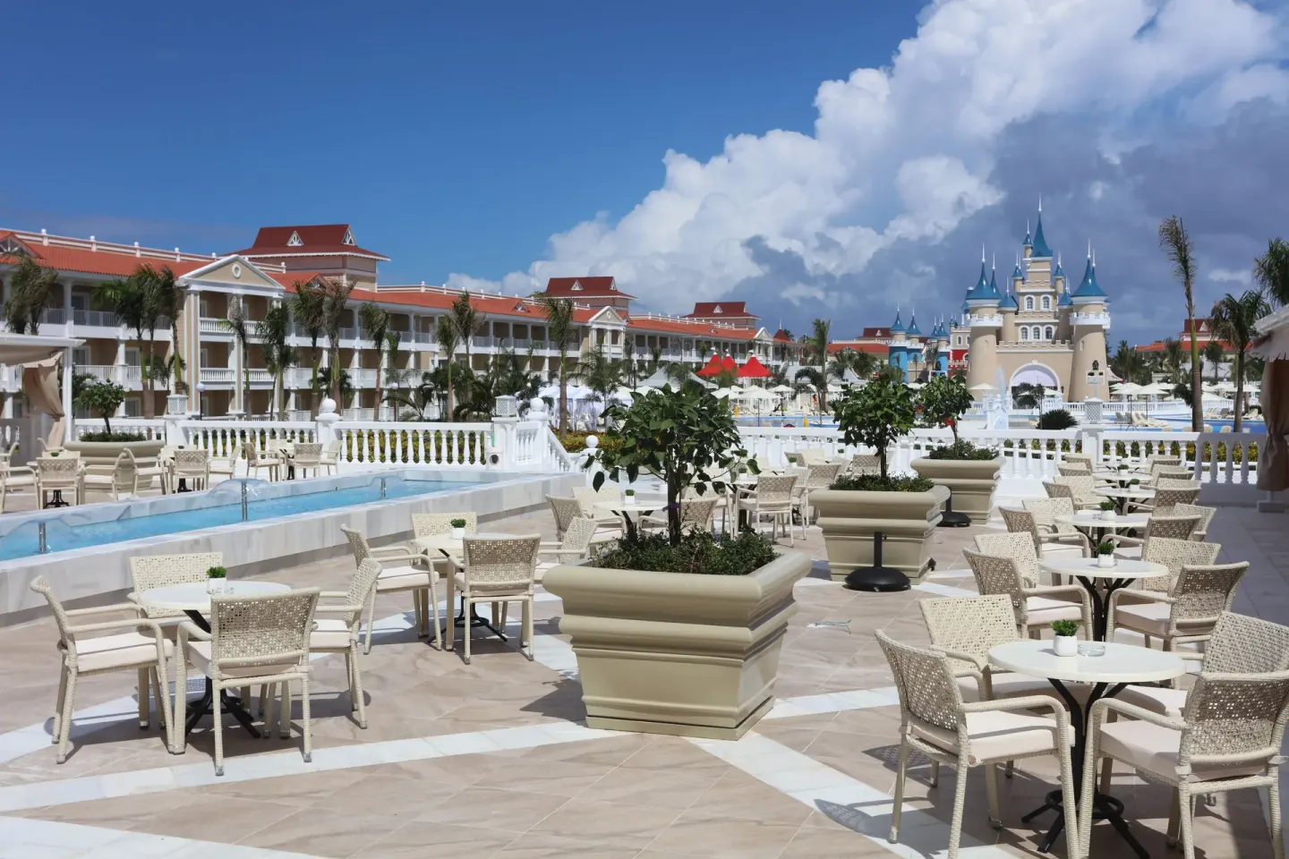 Outdoor terrace at Bahia Principe Explore Legend with café tables, pool water, and resort buildings.