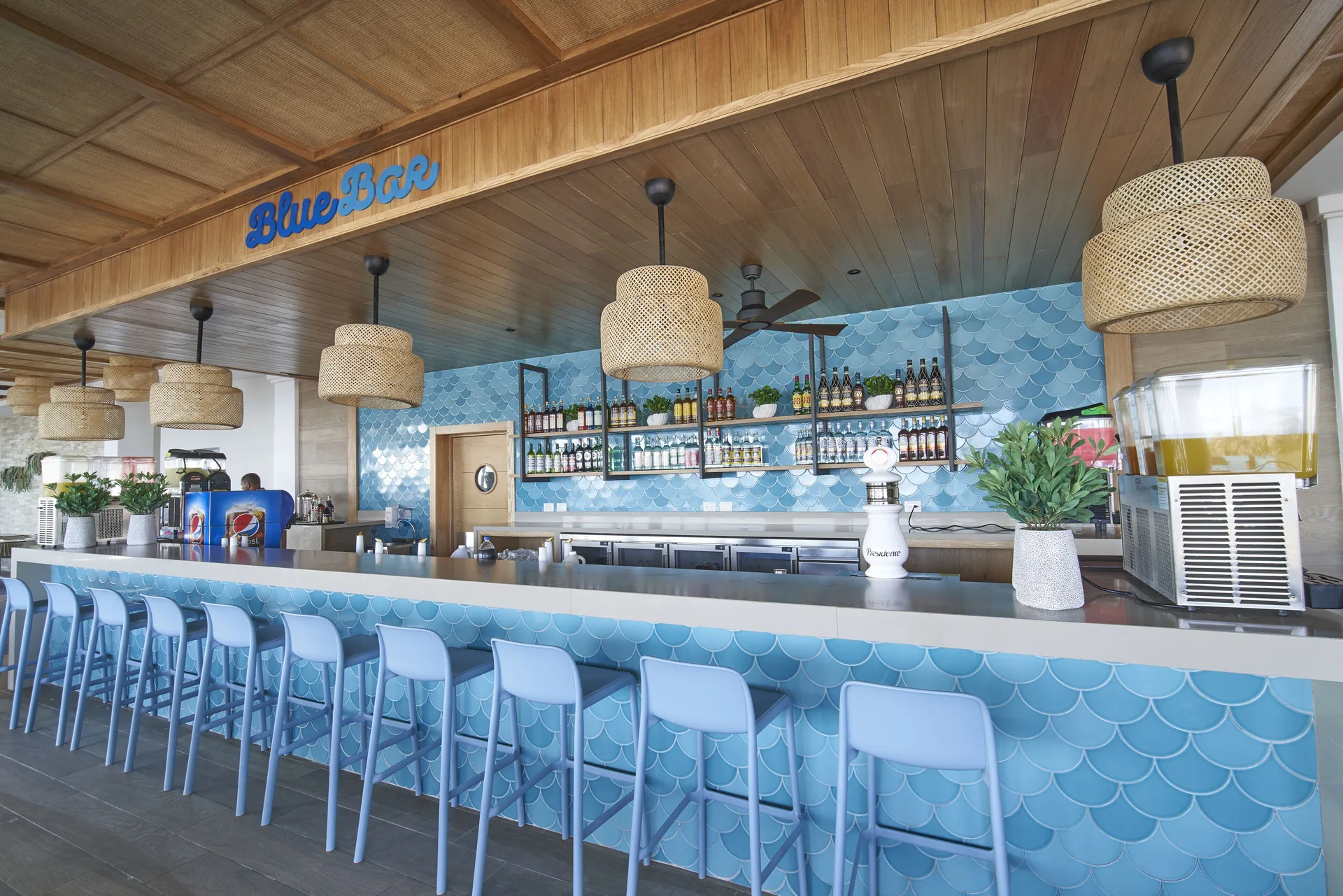 Blue-tiled bar with stools, hanging lights, and bottle shelves at Bahia Principe Explore Legend.