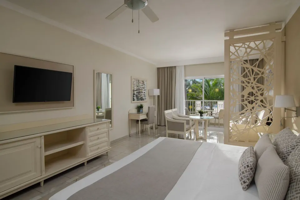 Junior Suite king bed, TV, and balcony seating at Bahia Principe Explore Legend.