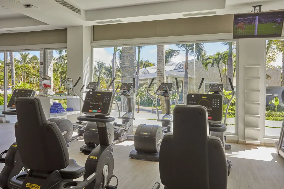 Exercise bikes and cardio machines face garden windows at Bahia Principe Grand Aquamarine.