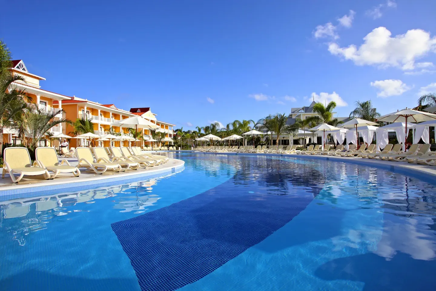 Large blue pool lined with loungers and umbrellas at Bahia Principe Grand Aquamarine.