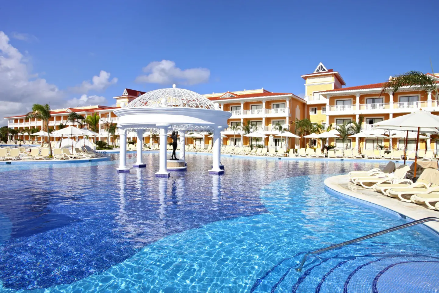 Pool with a white domed pavilion and surrounding loungers at Bahia Principe Grand Aquamarine.