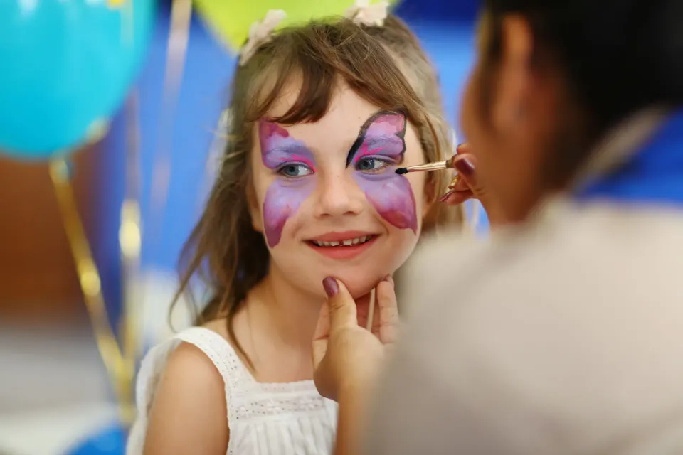 Girl having butterfly face paint applied at Bahia Principe Grand Coba kids activity