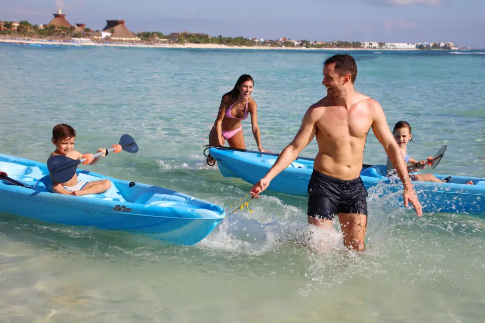 Family with kayaks splashing in shallow water at Bahia Principe Grand Coba