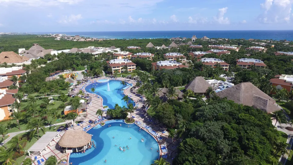 Aerial panorama of interconnected resort pools and thatched-roof structures at Bahia Principe Grand Coba