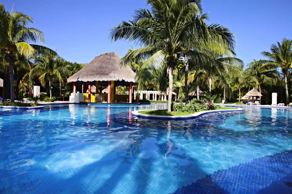 Pool-level view showing swim-up bar palapa and palm trees at Bahia Principe Grand Coba