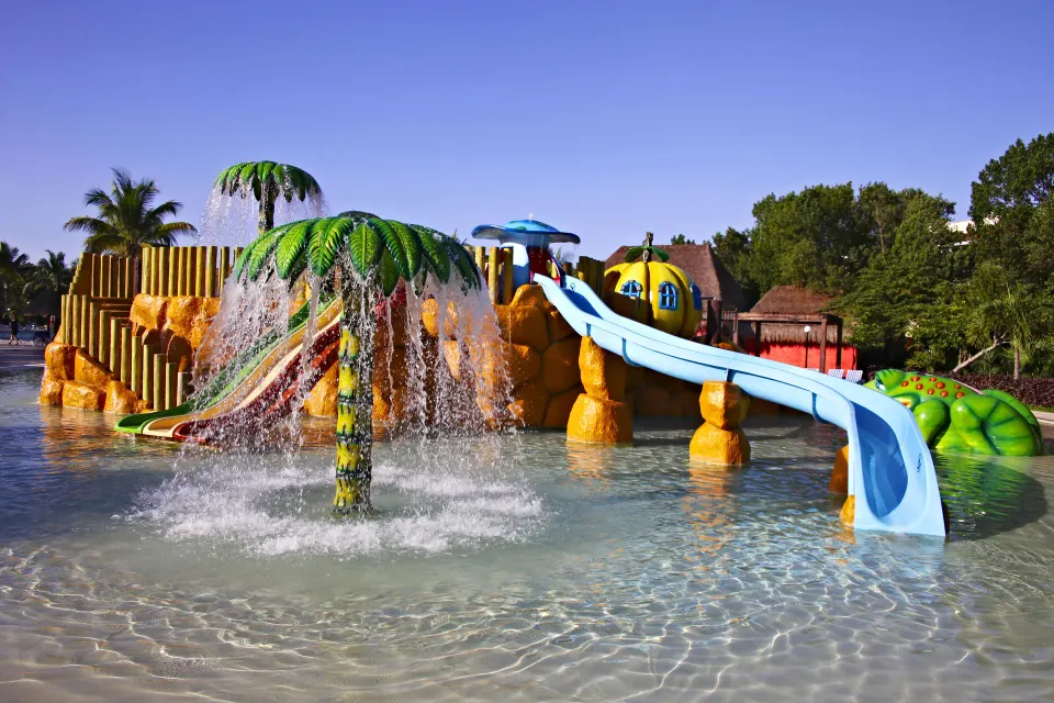 Close-up of water play area with palm fountain and blue slide at Bahia Principe Grand Coba