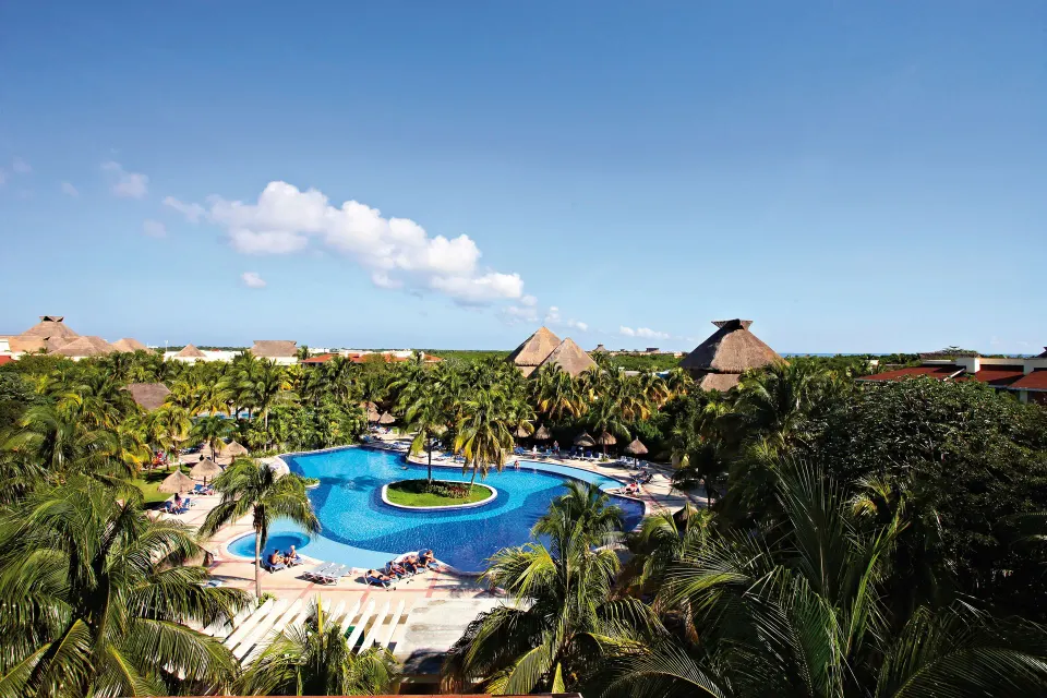 Overhead view of large resort pool surrounded by palm trees and thatched roofs at Bahia Principe Grand Coba