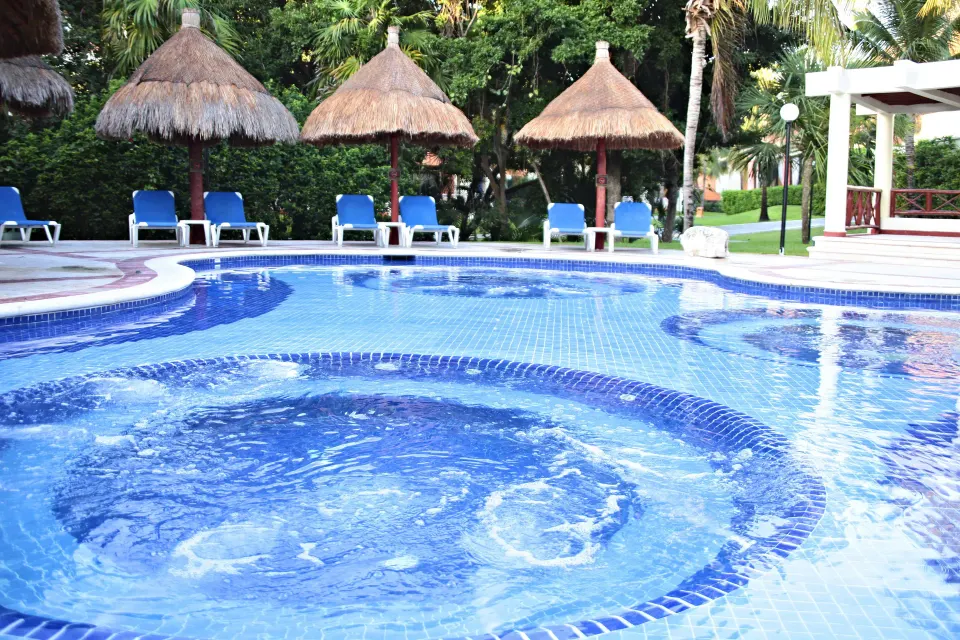 Curved outdoor pool and built-in whirlpool with palapa umbrellas at Bahia Principe Grand Coba.