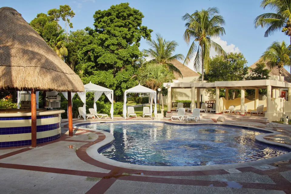 Quiet curved pool with thatched palapa, cabanas and loungers at Bahia Principe Grand Coba