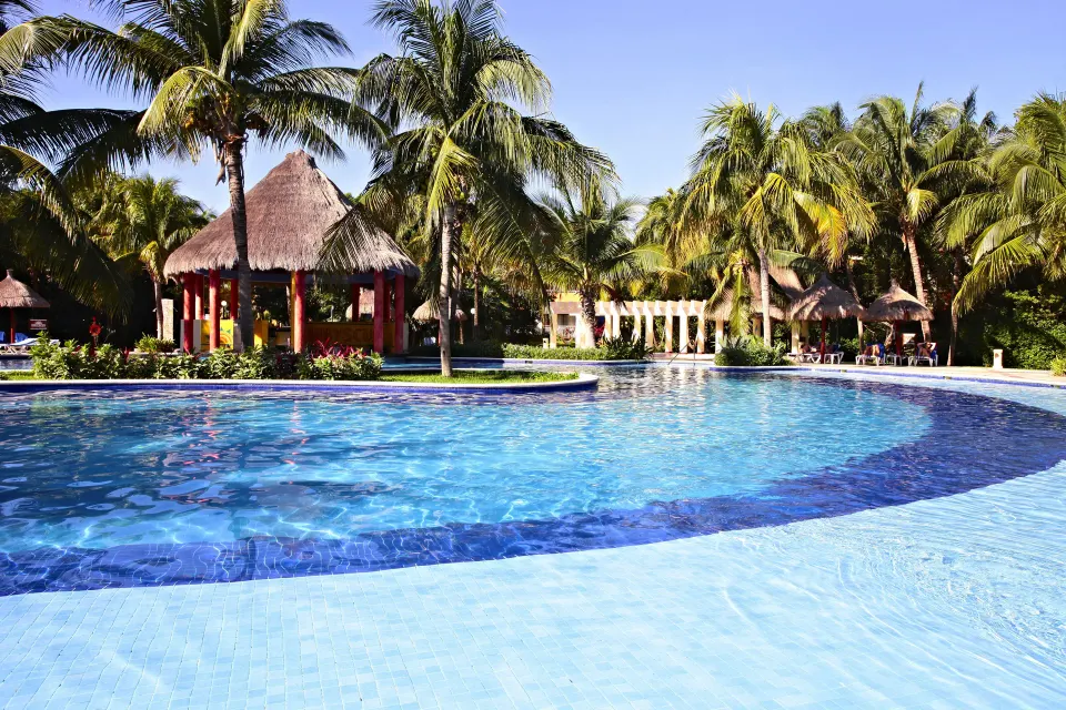 Wide shallow edge of the resort pool with palapa gazebo and palm trees at Bahia Principe Grand Coba