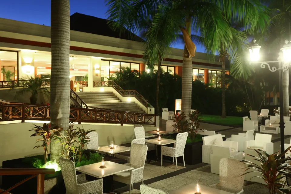 Lit outdoor dining and lounge area at night at Bahia Principe Grand Coba