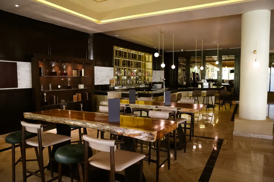 Modern indoor bar area with wood tables and stools at Bahia Principe Grand Coba