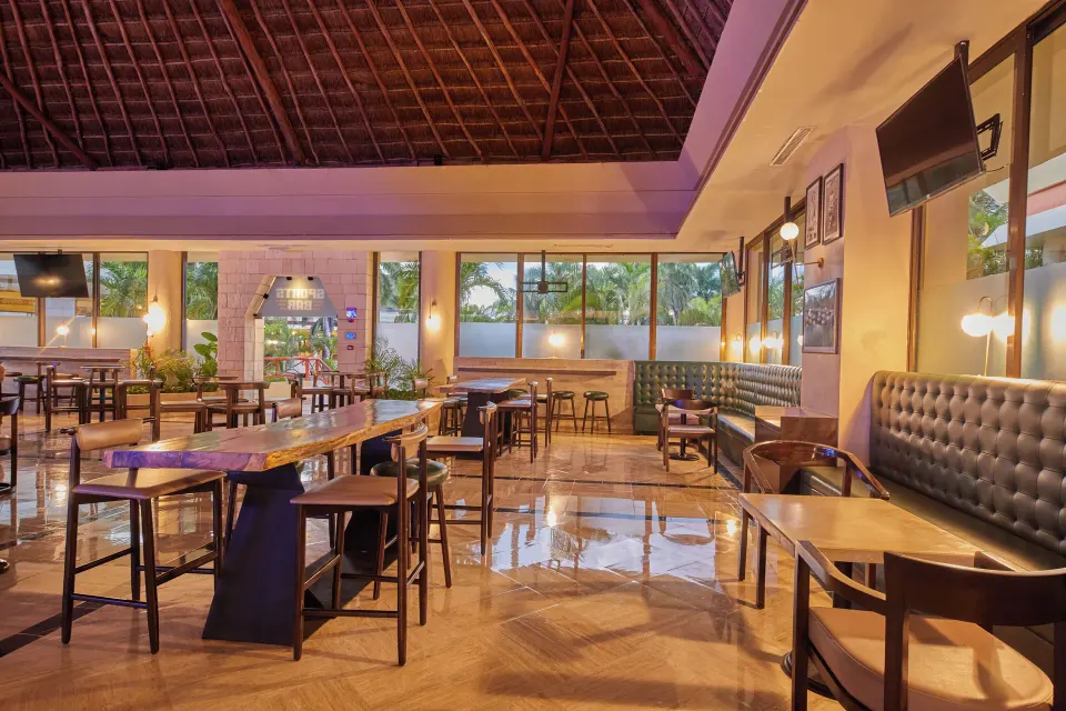 Casual restaurant seating with high tables under a palapa roof at Bahia Principe Grand Coba