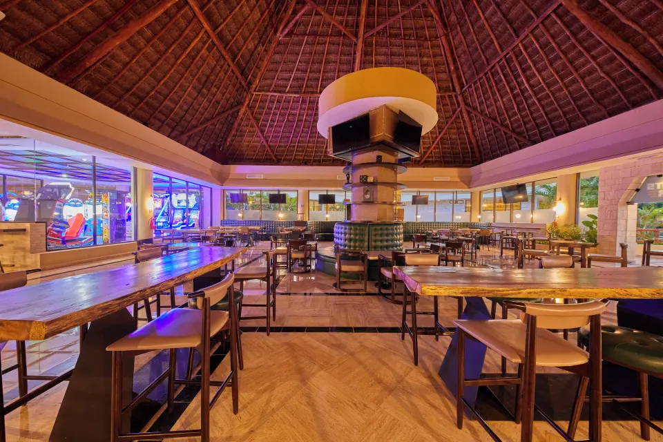 Thatched-roof palapa dining area with high tables by the resort at Bahia Principe Grand Coba