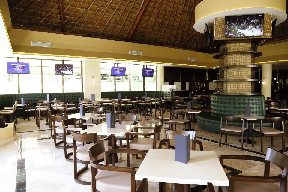 Casual sports bar seating with TVs and tables at Bahia Principe Grand Coba