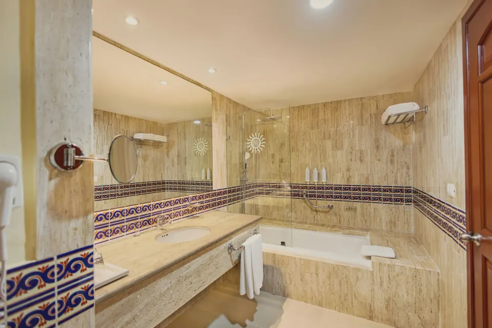 Bathroom corner showing bathtub, mirror and mounted hair dryer in a junior suite at Bahia Principe Grand Coba