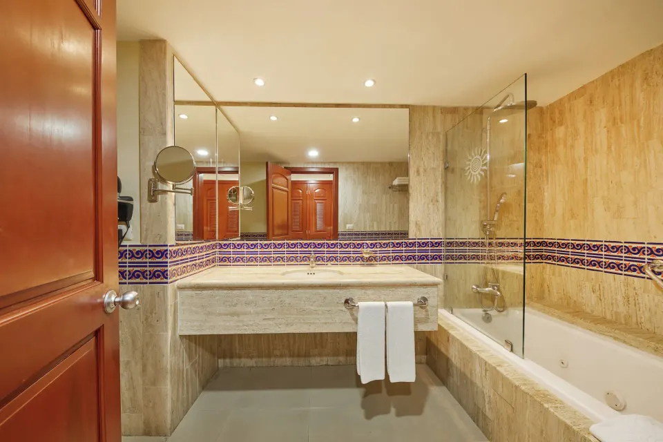 Bathroom with vanity, mirror and tub with glass partition in a junior suite at Bahia Principe Grand Coba