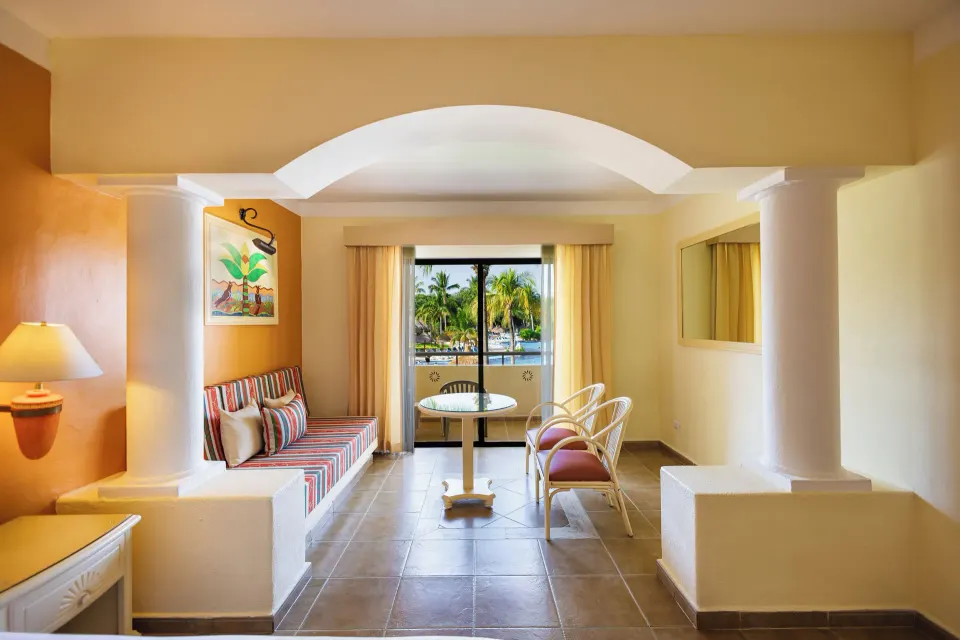 Seating area with banquette, table and balcony view in a junior suite at Bahia Principe Grand Coba