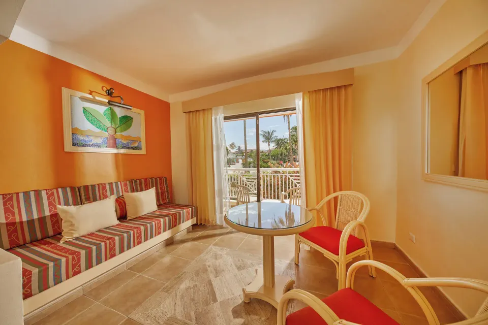 Sitting area with striped banquette and glass table facing balcony at Bahia Principe Grand Coba