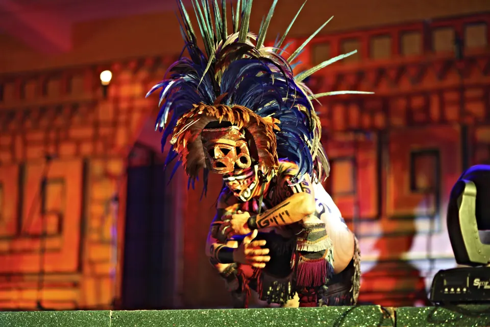 Costumed performer in an elaborate feathered headdress on stage at Bahia Principe Grand Coba