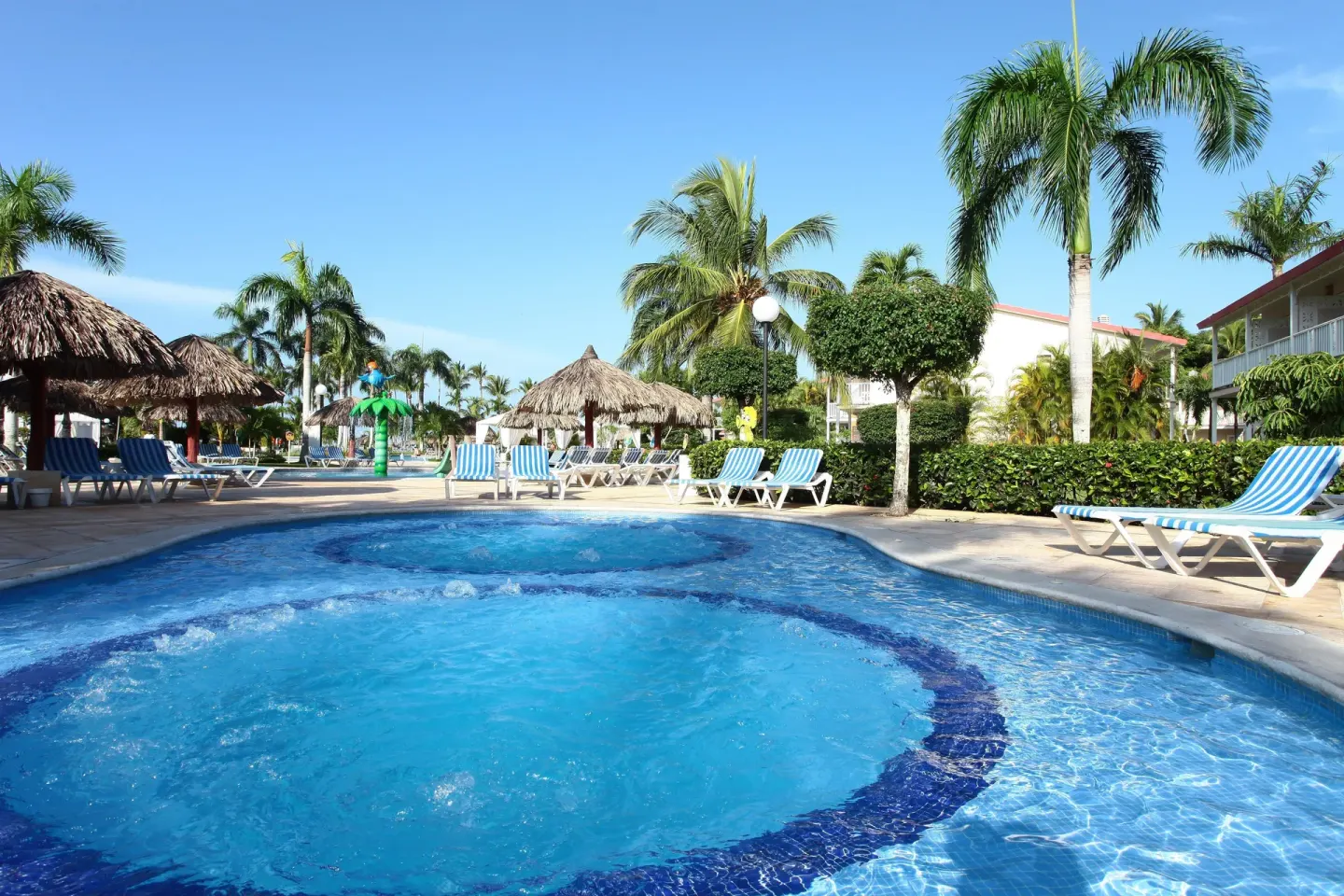 Bubbling pool area with loungers and thatched palapas at Bahia Principe Grand La Romana.
