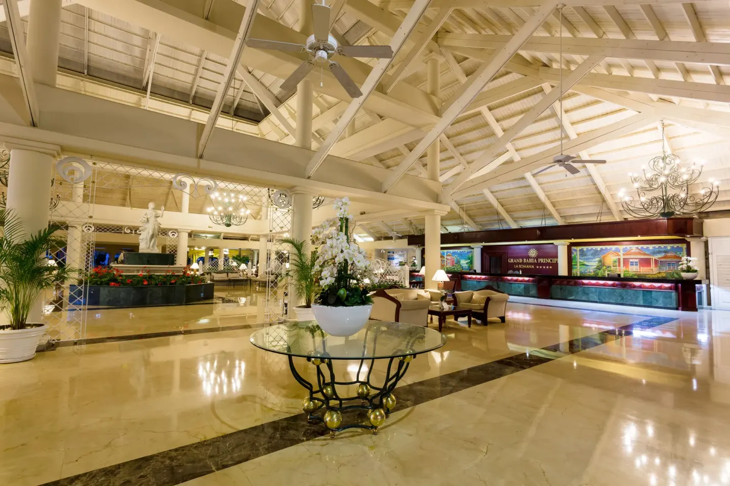 Grand lobby at Bahia Principe Grand La Romana with reception desk, chandeliers and floral table display.