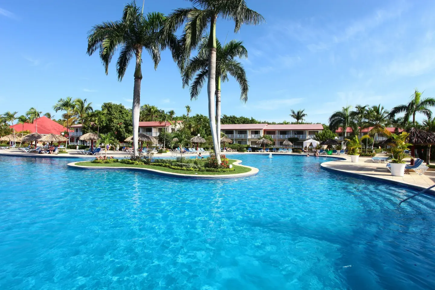 Bright blue pool with palm islands and guest buildings at Bahia Principe Grand La Romana.