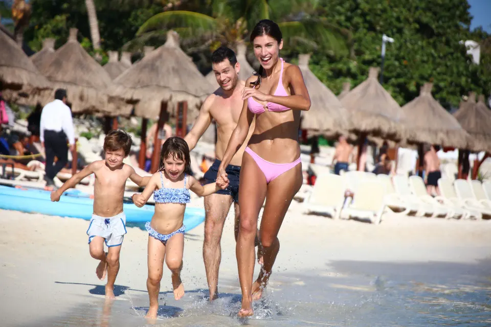 Family running on the beach at Bahia Principe Grand Tulum with palapas in background