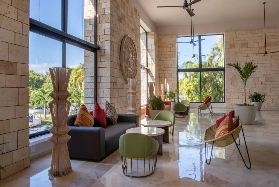 Sunlit lobby seating area with tall windows and colorful cushions at Bahia Principe Grand Tulum