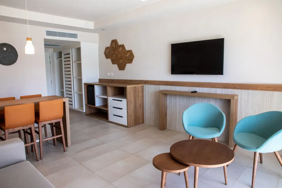 Seating area with TV and turquoise chairs in a suite at Bahia Principe Grand Tulum
