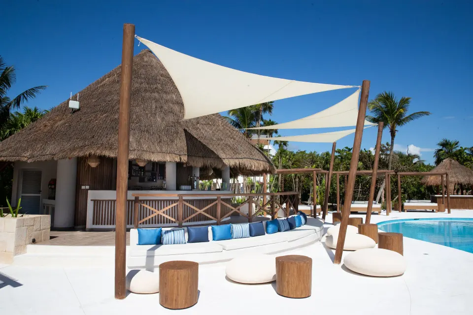 Thatched pool bar seating and shaded lounges beside a pool at Bahia Principe Grand Tulum