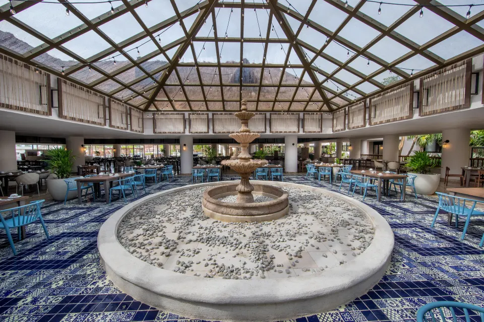 Indoor restaurant seating around a tiled fountain under skylight at Bahia Principe Grand Tulum