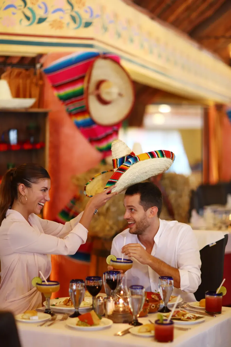 Couple enjoying a festive meal with sombrero hat at Bahia Principe Grand Tulum