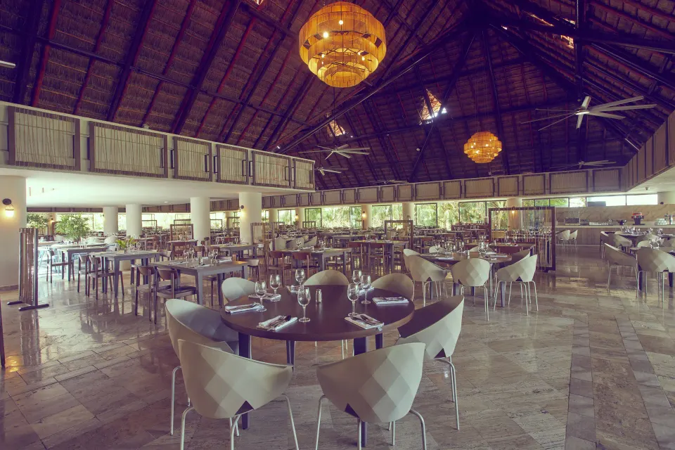 Large palapa dining hall with rows of tables and high ceiling at Bahia Principe Grand Tulum