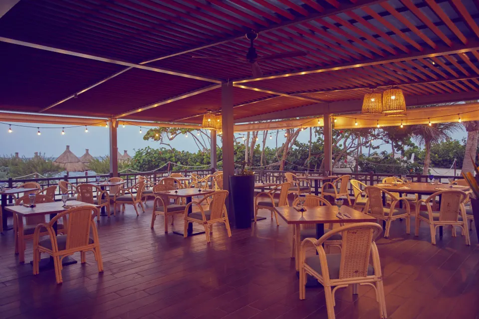 Covered terrace dining area with ocean glimpses and wicker chairs at Bahia Principe Grand Tulum