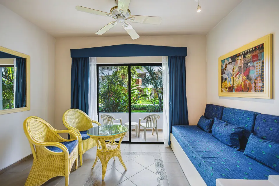 Junior Suite sitting area with wicker chairs, blue sofa and balcony at Bahia Principe Grand Tulum