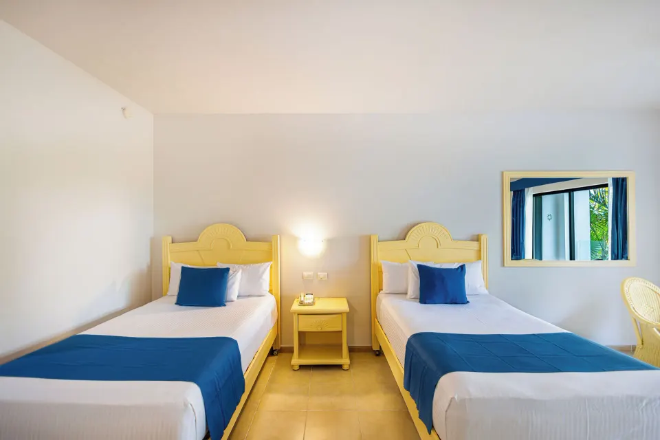 Twin beds with blue accents and nightstand in a Junior Suite at Bahia Principe Grand Tulum