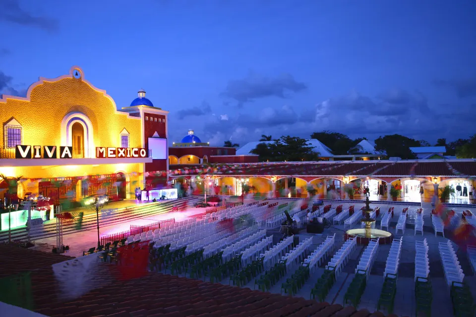 Outdoor event plaza with rows of chairs and a lit Viva Mexico facade at night at Bahia Principe Grand Tulum.