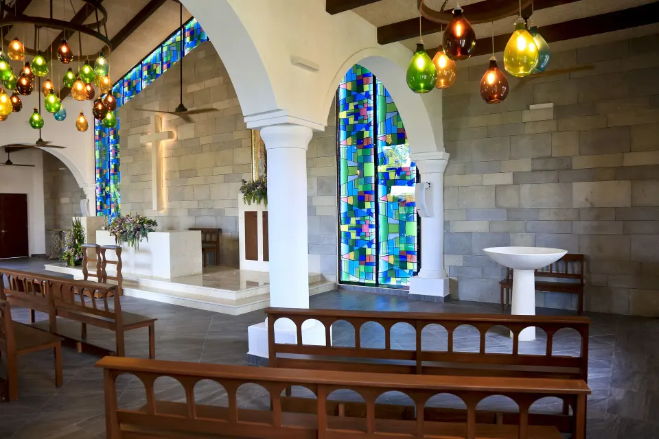 Small chapel interior with stained glass and wooden pews at Bahia Principe Grand Tulum