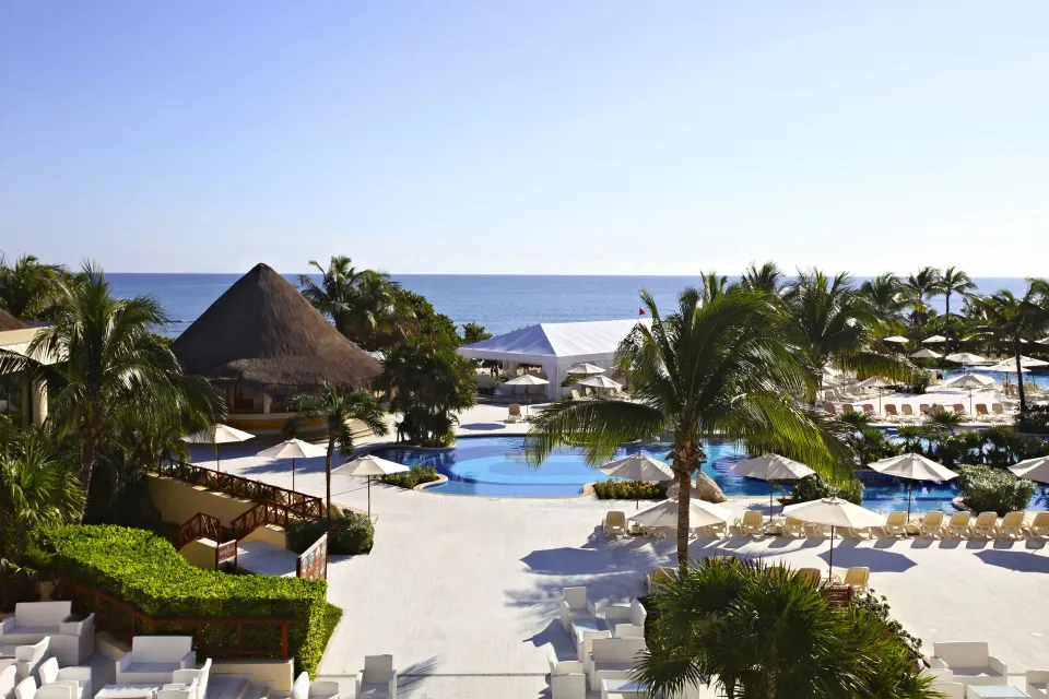 Pool and beachfront scene with palapa structures at Bahia Principe Luxury Akumal.