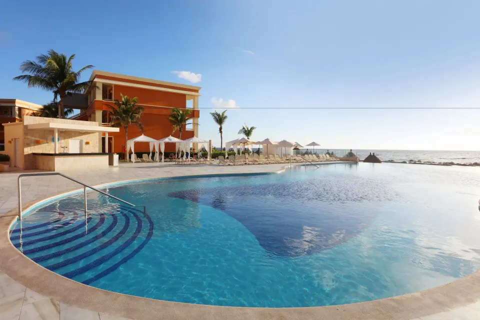 Curved beachfront pool with adjacent orange building at Bahia Principe Luxury Akumal.