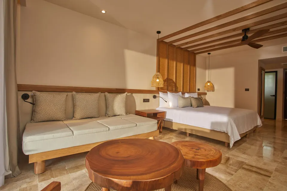 King bed and cushioned bench with wooden coffee tables in a room at Bahia Principe Luxury Akumal.