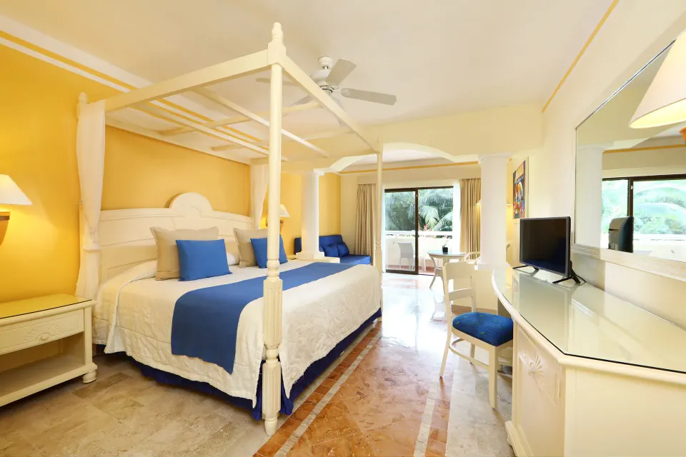 Canopy king bed with blue accents and patio doors in a guest room at Bahia Principe Luxury Akumal